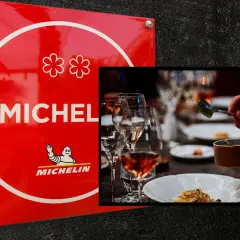 Czerwona tablica z dwoma kwiatkami symbolizującymi gwiazdkę Michelin. Obok elegancko nakryty stół, gdzie kucharz serwuje danie.