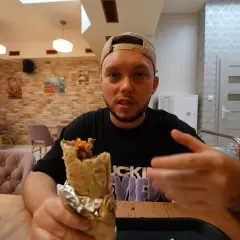 Mężczyzna z kebabem w ręku, prawdopodobnie najlepszy kebab warszawa. Wnętrze restauracji z ceglanymi ścianami i wygodnymi fotelami.
