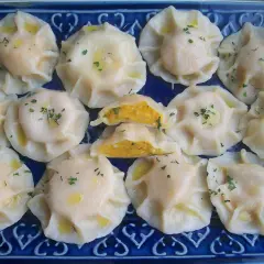 Pyszne pierogi z dynią, polane masłem i posypane natką pietruszki, ułożone na niebieskiej tacy.