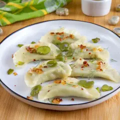 Pyszne pierogi z bobem, posypane skwarkami i koperkiem, prezentują się apetycznie na talerzu.