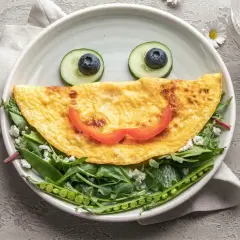 Uśmiechnięta omletowa buzia z oczami z ogórka i borówki, ułożona na sałatce z groszkiem. Idealny comfort food na dobry początek dnia.