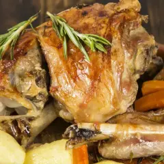 Pyszne dania z baraniny: pieczone kawałki mięsa z ziemniakami i marchewką, ozdobione rozmarynem.