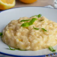 Kremowe risotto cytrynowe, ozdobione listkami bazylii, na talerzu z cytryną w tle.