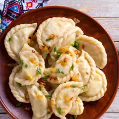 Pyszne pierogi z bryndzą, posypane skwarkami i szczypiorkiem, podane z łyżką śmietany.