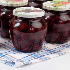 Słoiki pełne kompotu z czereśni, gotowe na zimę. Ciemne owoce w słodkim syropie kuszą smakiem.