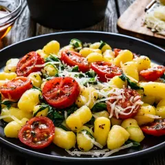 Pyszne gnocchi szpinakowe z pomidorkami koktajlowymi i parmezanem na drewnianym stole.