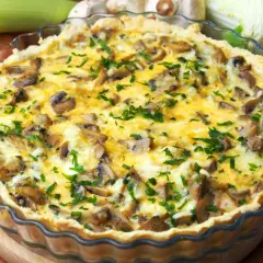 Pyszna tarta z pieczarkami i porem, posypana świeżą natką pietruszki, w szklanej formie.