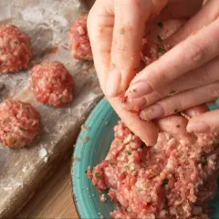 Ręce formują klopsiki według przepisu na meatballs. Na desce widać już gotowe, obtoczone w mące kulki mięsa.