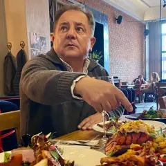 Robert Makłowicz wskazuje na obficie zastawiony stół w restauracji. Widać dania z owocami morza i mięsem.