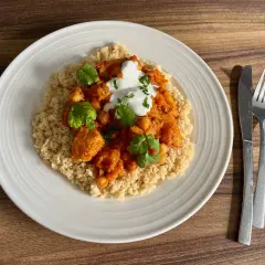 Tagine z kurczakiem i ciecierzycą na kuskusie, udekorowane jogurtem i kolendrą.