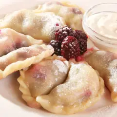 Pyszne pierogi z malinami, posypane cukrem pudrem, podane z kwaśną śmietaną i świeżymi owocami leśnymi.