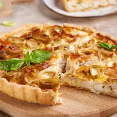 Pyszna tarta z jarmużem, kurczakiem i porami, udekorowana listkami bazylii, prezentuje się apetycznie na drewnianej desce.