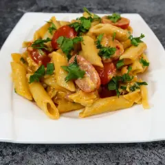 Penne z kremowym sosem serowym, kawałkami chrupiącego boczku i pomidorkami koktajlowymi, posypane świeżą natką pietruszki.