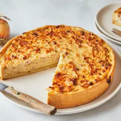 Pyszna tarta cebulowa z chrupiącym spodem i kremowym nadzieniem, gotowa do podania. Obok leżą świeże cebule.