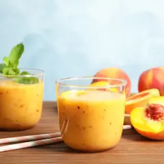 Dwa szklanki orzeźwiającego koktajlu brzoskwiniowego z miętą, obok świeżych brzoskwiń. Idealny na lato!