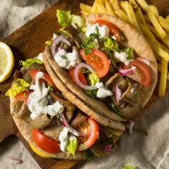 Pyszny grecki gyros z kawałków mięsa opiekanego na rożnie, podany z frytkami, warzywami i sosem.