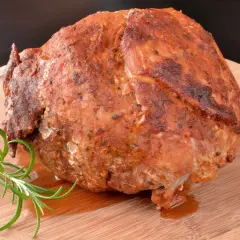 Soczysta, aromatyczna szynka pieczona, przyprawiona ziołami, leży na drewnianej desce z gałązką rozmarynu.