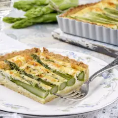 Pyszna tarta ze szparagami, z chrupiącym spodem i kremowym nadzieniem, podana na talerzyku z delikatnym wzorem.