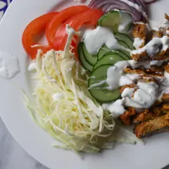 Na talerzu świeże składniki kebaba: pokrojony kurczak, kapusta, pomidor, ogórek, cebula i sos.