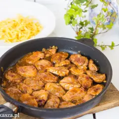 Polędwiczki w sosie miodowo musztardowym w patelni, obok talerz makaronu. Pyszne danie gotowe do podania.