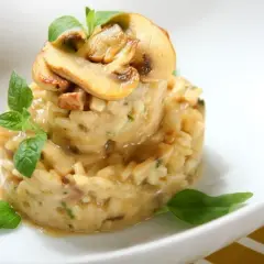 Aromatyczne risotto z boczniakami, udekorowane świeżymi ziołami i plasterkami grzybów, prezentuje się apetycznie na białym talerzu.