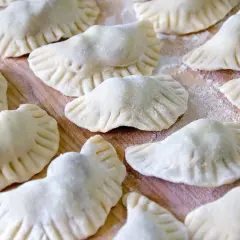 Surowe pierogi z kaszą gryczaną ułożone na drewnianej desce, posypane mąką.