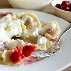 Pyszne pierogi z wiśniami, polane gęstą śmietaną, kuszą soczystym nadzieniem. Idealne na deser lub słodki obiad.