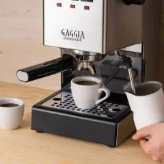 Gaggia Classic przygotowuje aromatyczną kawę do ekspresu ciśnieniowego. Na blacie stoi filiżanka z czarnym napojem, a obok dzbanek do spieniania mleka.