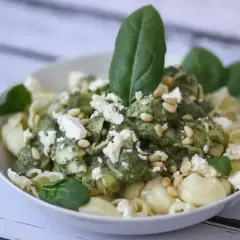 Pyszny makaron z fetą, polany zielonym pesto i posypany orzeszkami pinii. Idealny na szybki obiad.