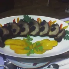 Apetyczna mięsna plata z plastrami żółtej papryki i czarnymi oliwkami, ozdobiona natką pietruszki.