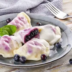 Pyszne pierogi z jagodami, polane śmietaną, ozdobione miętą i świeżymi owocami. Idealne na deser!