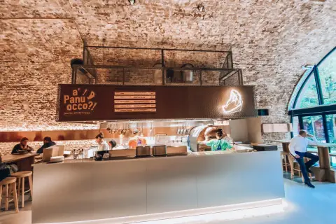 Wnętrze jednej z nowych restauracji w Warszawie. Widać piec do pizzy, bar i gości.