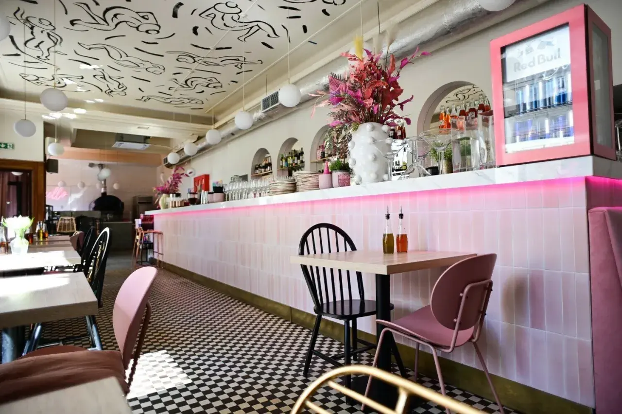 Stylowe wnętrze restauracji w Warszawie z różowym neonem i czarno-białą szachownicą na podłodze. Idealne miejsce na listę "top 10 restauracji Warszawa".