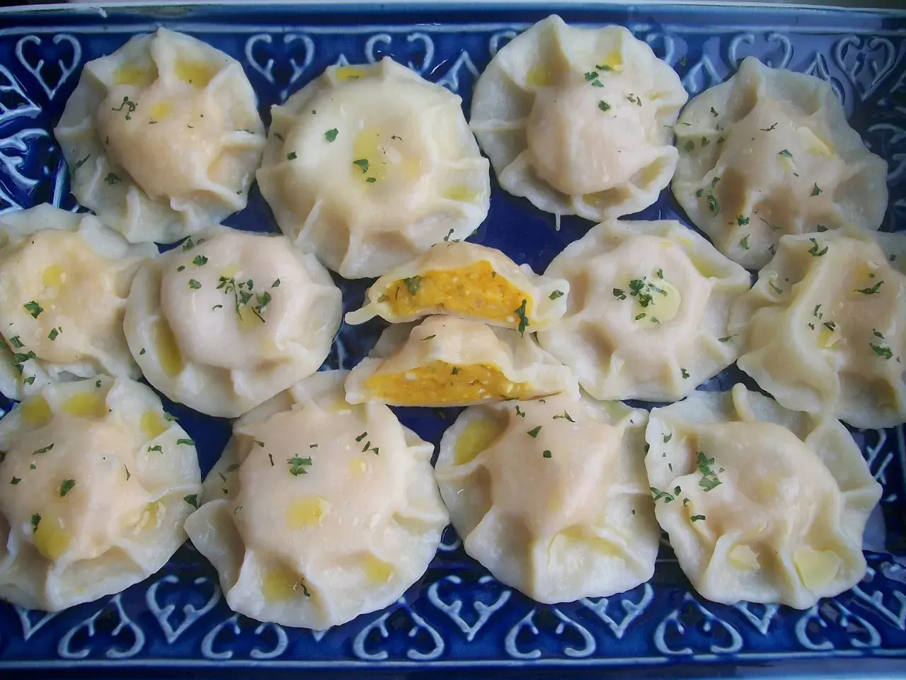 Pyszne pierogi z dynią, polane masłem i posypane natką pietruszki, ułożone na niebieskiej tacy.