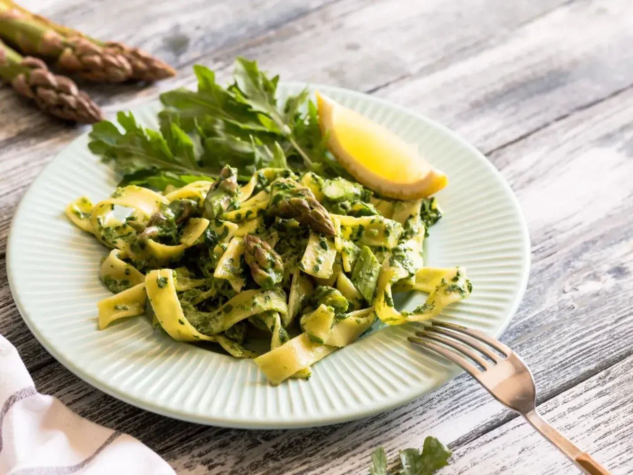 Pappardelle z zielonym sosem, szparagi i rukola na talerzu. Pyszny makaron ze świeżymi warzywami.