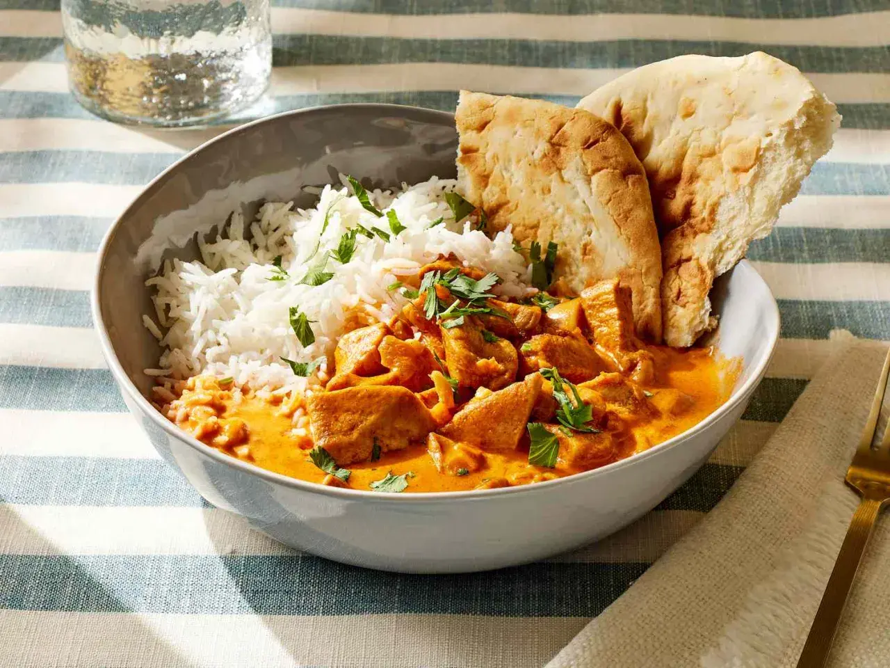 Miseczka pełna aromatycznego kurczaka butter chicken z ryżem i chlebkiem naan.
