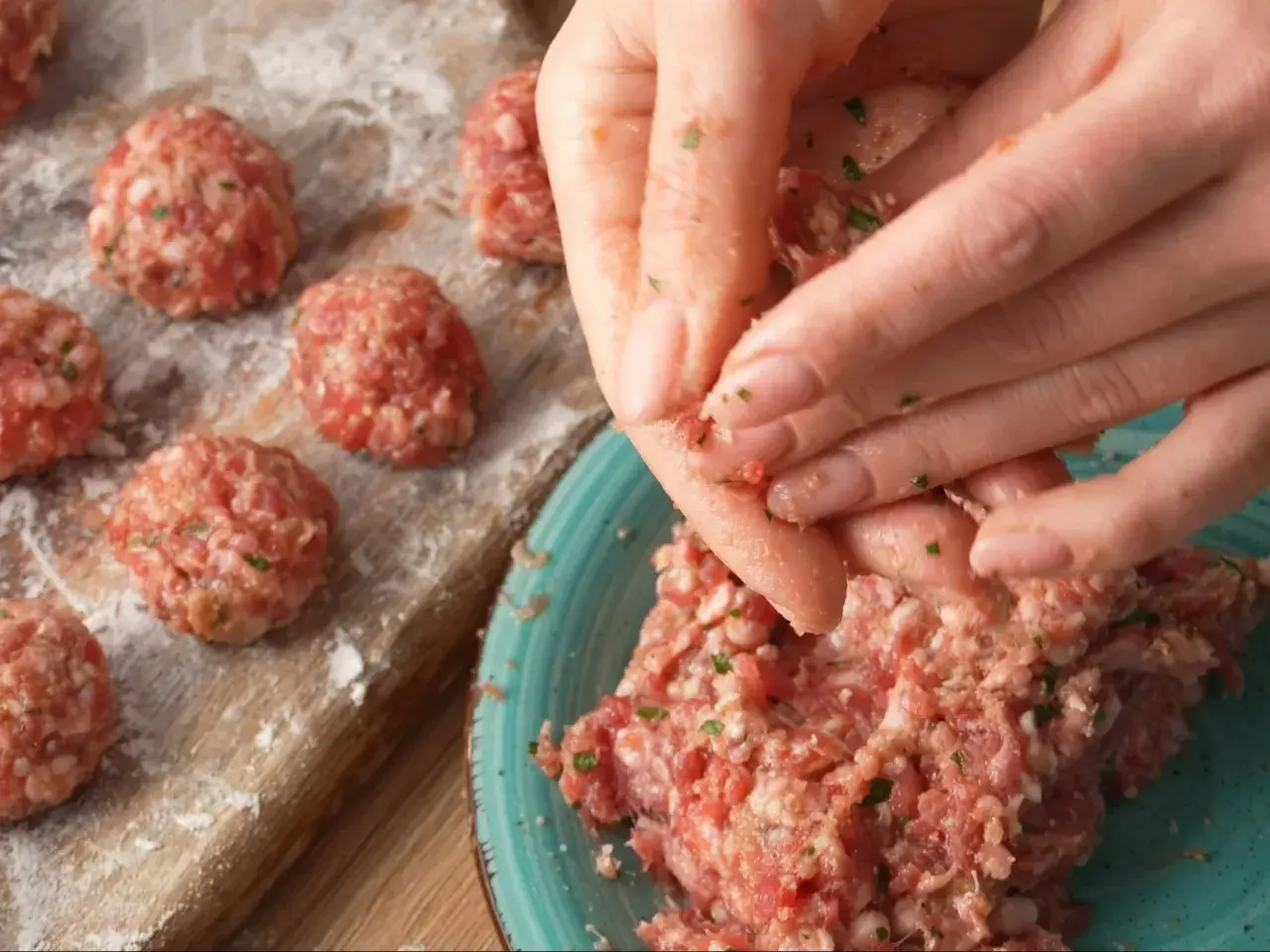 Ręce formują klopsiki według przepisu na meatballs. Na desce widać już gotowe, obtoczone w mące kulki mięsa.