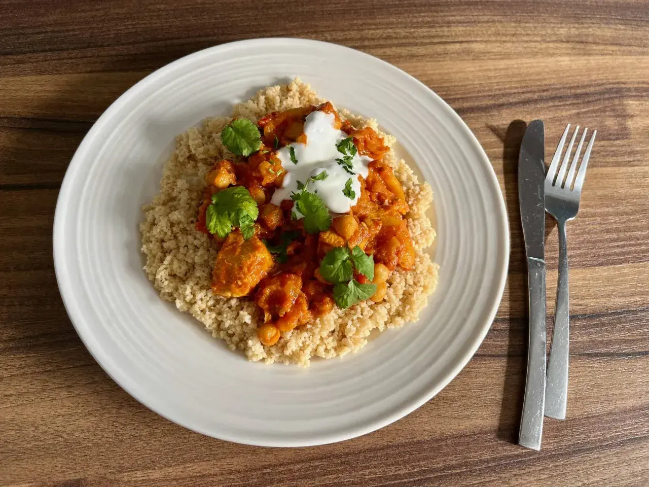 Tagine z kurczakiem i ciecierzycą na kuskusie, udekorowane jogurtem i kolendrą.