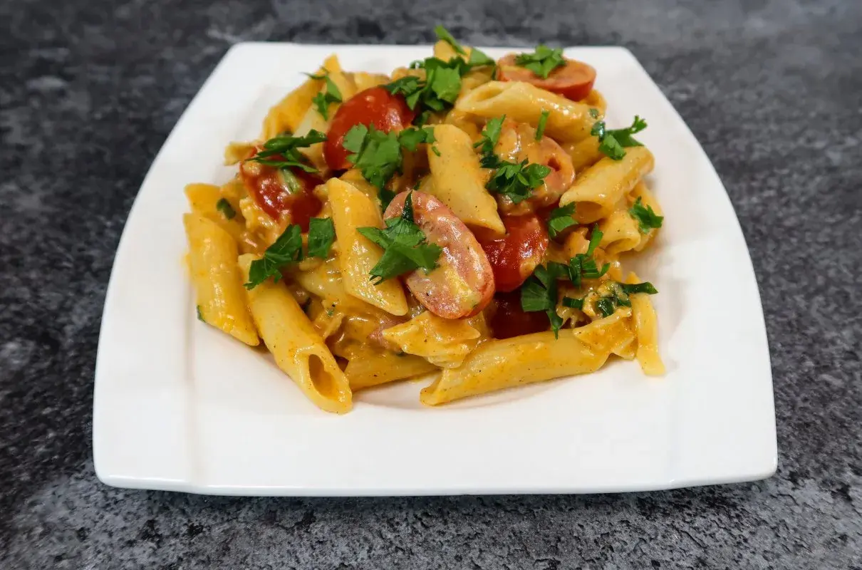 Penne z kremowym sosem serowym, kawałkami chrupiącego boczku i pomidorkami koktajlowymi, posypane świeżą natką pietruszki.