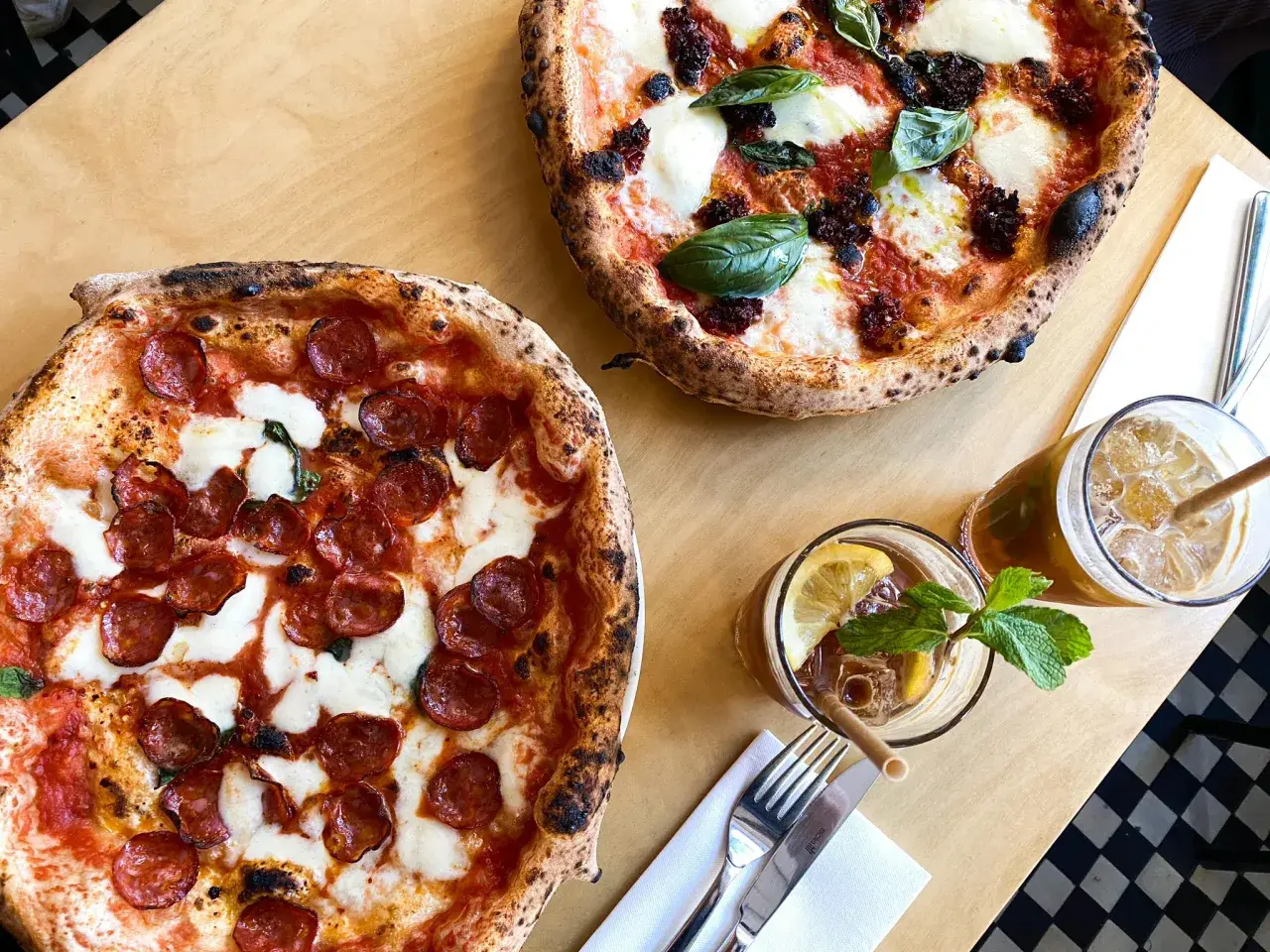 Dwie pyszne pizze, jedna z salami, druga z pomidorami i mozzarellą, idealne na najlepszą pizzę Warszawa. Do tego orzeźwiające napoje.