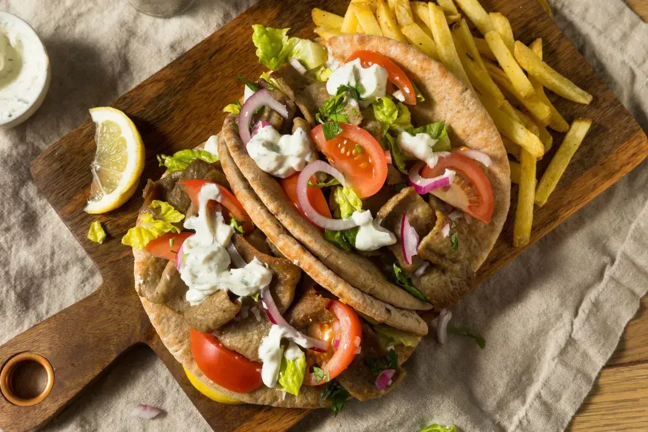 Pyszny grecki gyros z kawałków mięsa opiekanego na rożnie, podany z frytkami, warzywami i sosem.