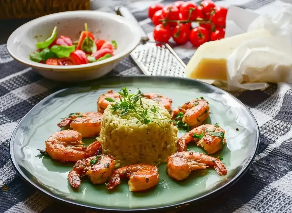 Krewetki z mlekiem kokosowym i curry na risotto, udekorowane ziołami. Obok miseczka z pomidorkami i bazylią, ser i tarka.