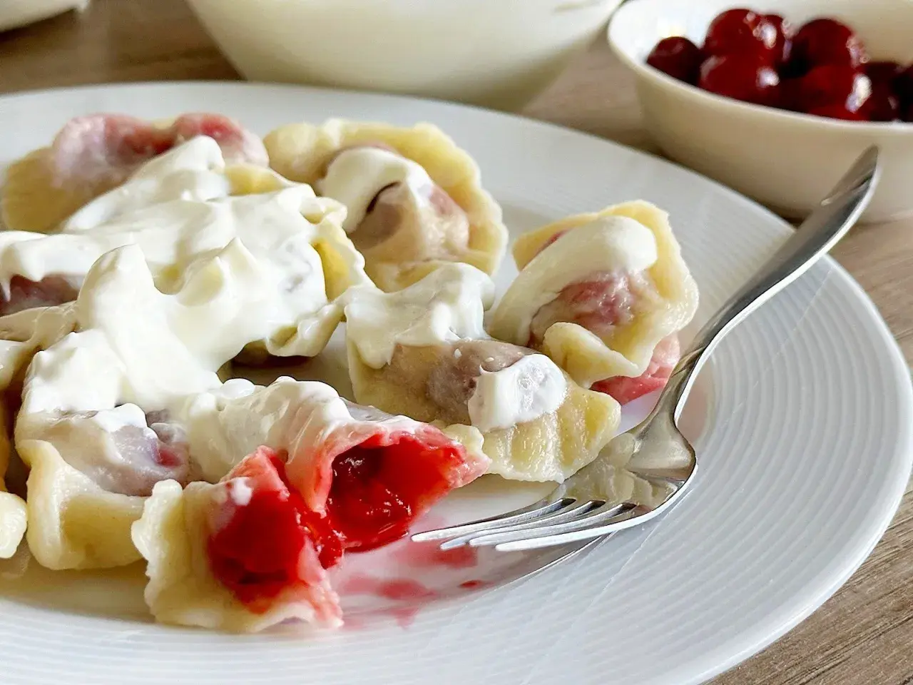 Pyszne pierogi z wiśniami, polane gęstą śmietaną, kuszą soczystym nadzieniem. Idealne na deser lub słodki obiad.