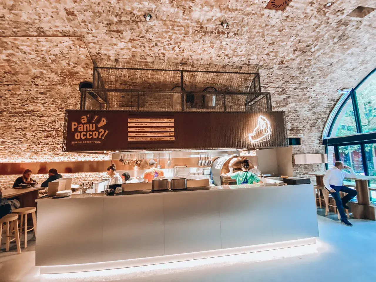 Wnętrze jednej z nowych restauracji w Warszawie. Widać piec do pizzy, bar i gości.