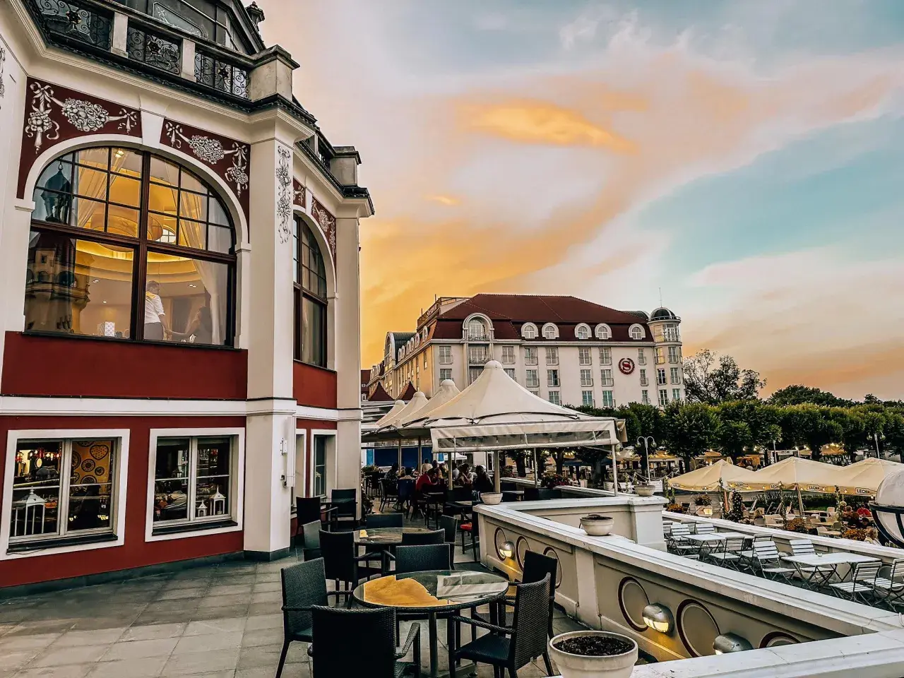 Eleganckie tarasy z widokiem na morze, idealne na kolację w jednej z nowych restauracji w Gdańsku. Zachód słońca maluje niebo na pomarańczowo.