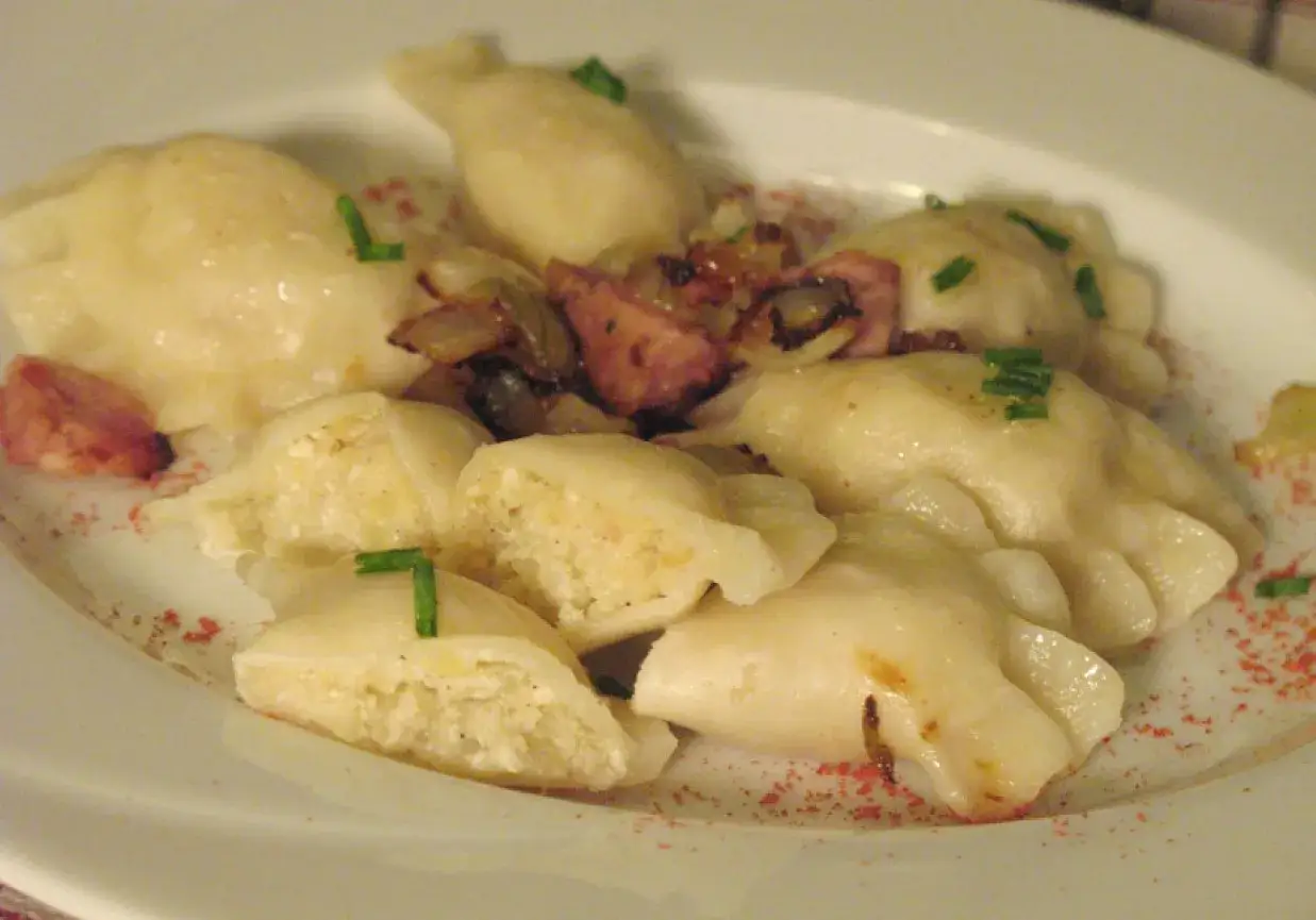 Pyszne pierogi z bryndzą, okraszone cebulką i boczkiem, posypane szczypiorkiem i papryką.