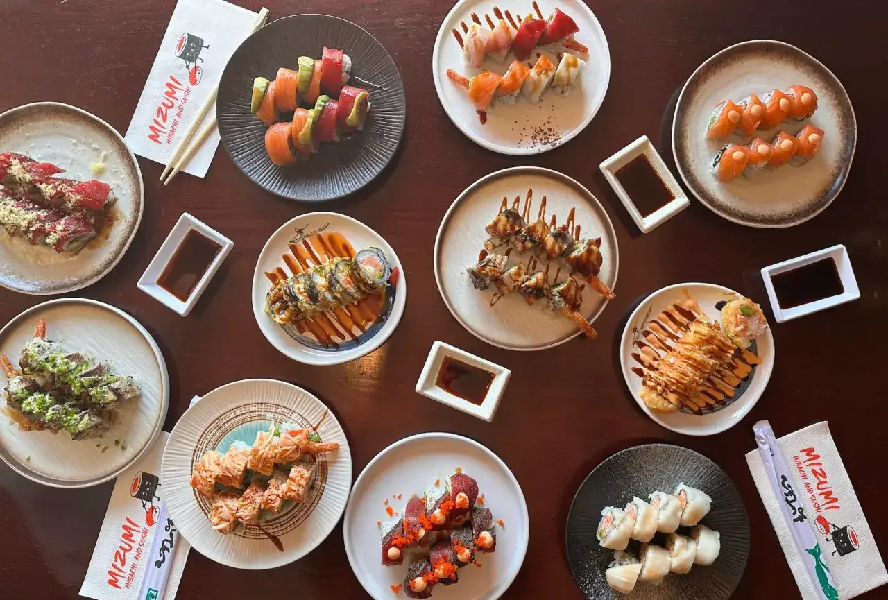 Różnorodne rolki sushi z menu Mizumi Hibachi and Sushi, podane na talerzach z sosami.