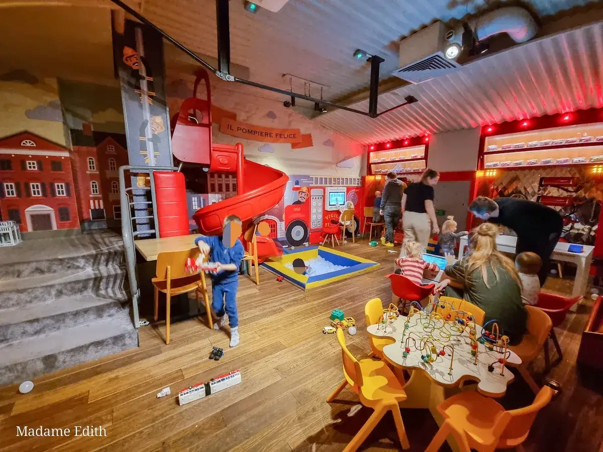Wesoła restauracja z bawialnią dla dzieci, gdzie maluchy mogą się bawić na zjeżdżalni i w basenie z kulkami, podczas gdy rodzice odpoczywają.
