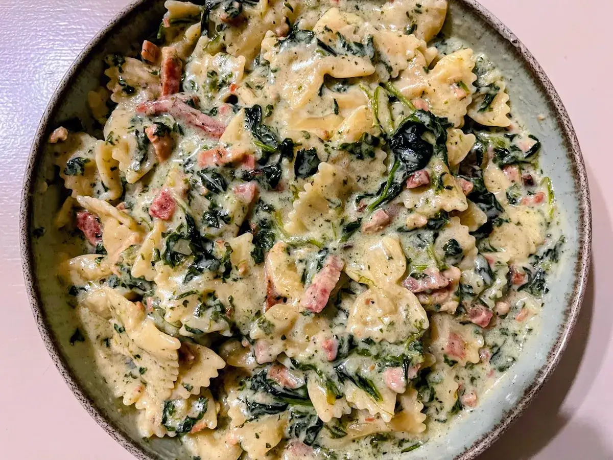 Pyszny makaron farfalle ze szpinakiem i kawałkami boczku w kremowym sosie. Idealny na szybki obiad.