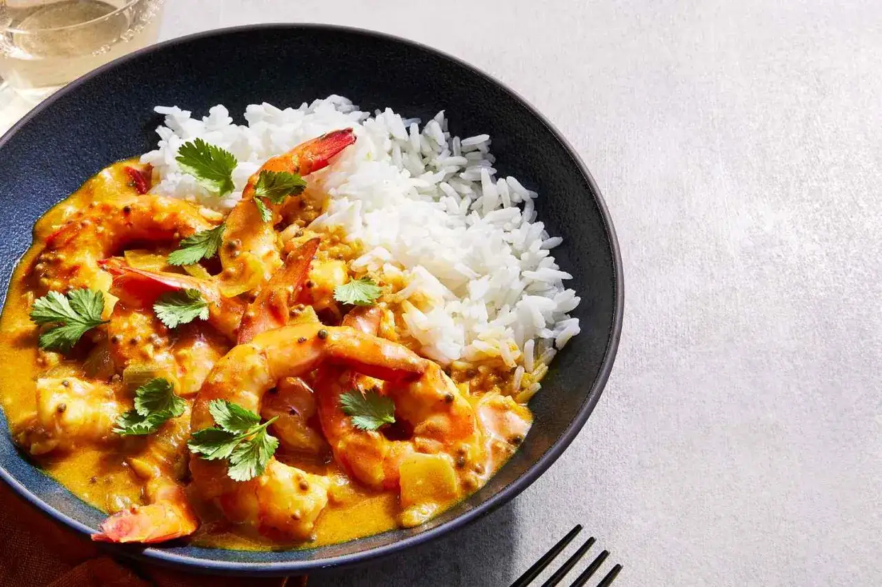 Krewetki w kremowym sosie curry z mlekiem kokosowym, podane z ryżem i świeżą kolendrą. Pyszne danie pełne smaku.